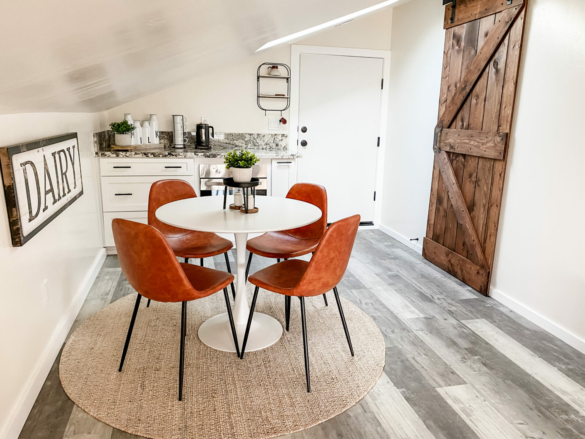 Dining Area of the Dairy Sweet with leather chairs, an oven and coffee bar shown. The decor is rustic with a sliding barn door, but also light and clean.